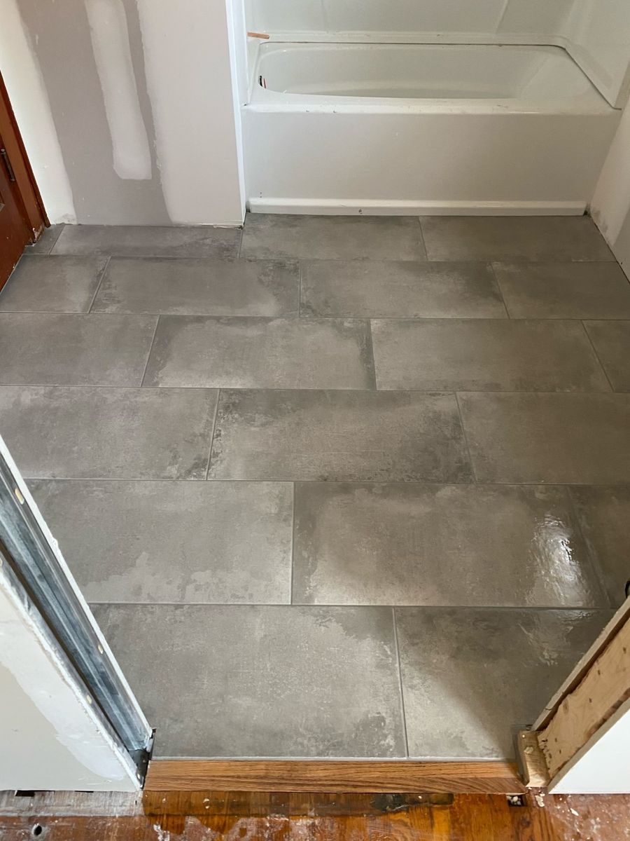 Bathroom floor in large-format gray tile beside a white tub