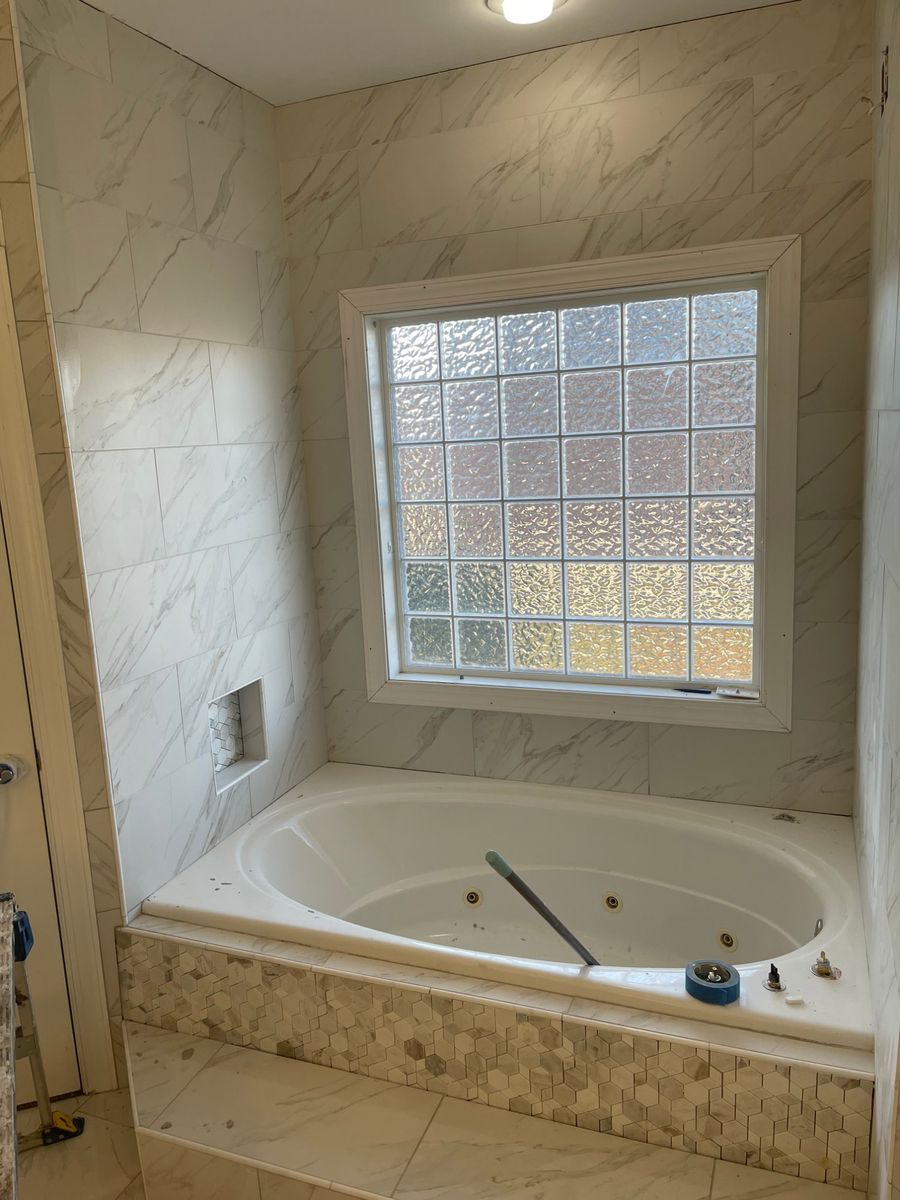 Soaking tub with marble-look tile surround, hexagon mosaic skirt, and tiled niche