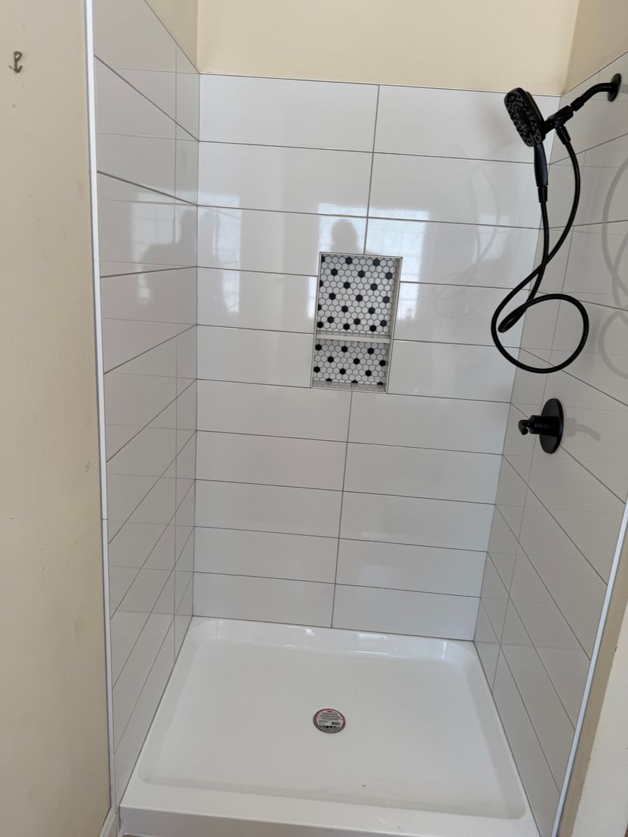 White tile shower with black-and-white hexagon niche and matte black fixtures